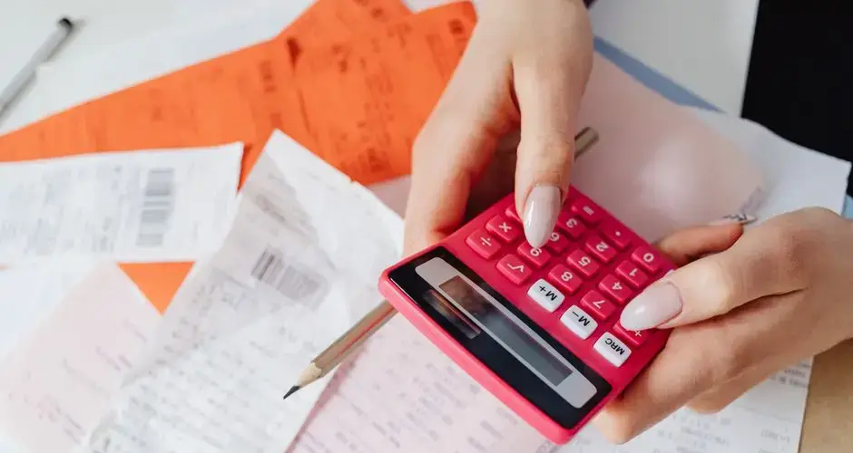 Hands using a pink calculator to manage expenses amidst various receipts and documents.