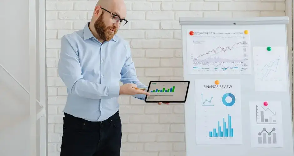 Man presenting financial data on tablet and charts indoors.
