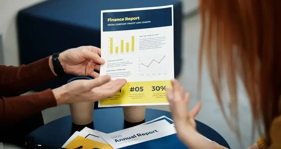 Two individuals analyzing a finance report chart at a business meeting in an office setting.