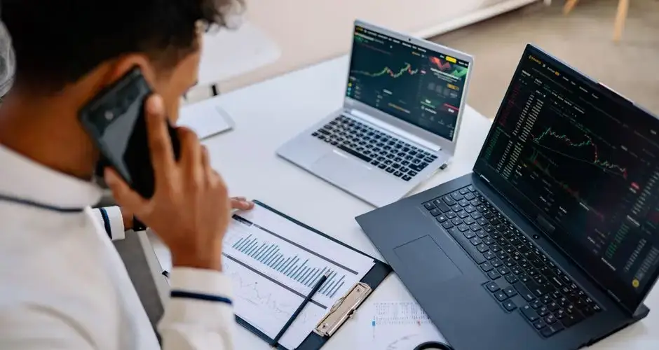 Man analyzing stock market charts on laptops while talking on a cellphone.