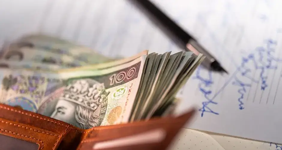 Stack of Polish zloty banknotes with pen and document, financial concept.