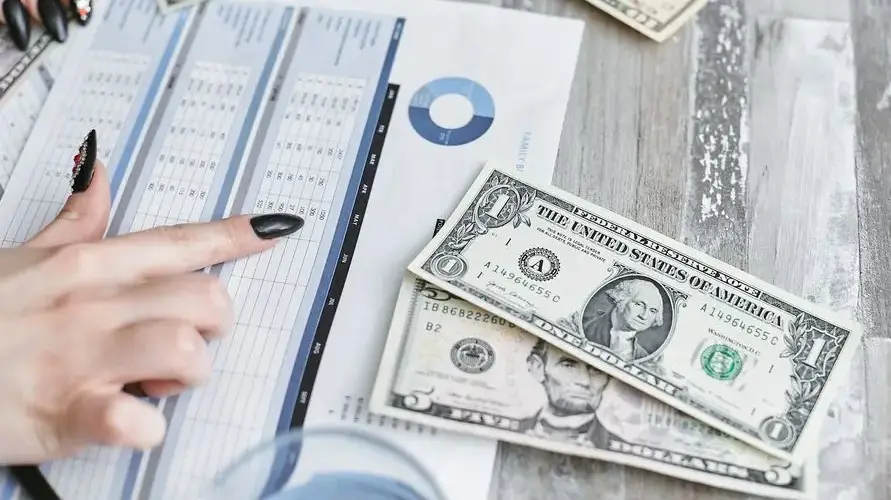 Close-up of hands analyzing financial document with US dollar bills on table.