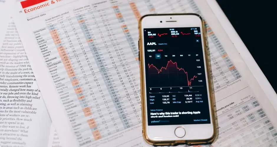 Smartphone displaying stock market data on papers with financial charts.