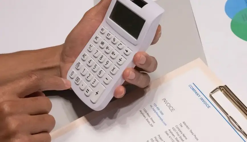 Close-up of hands using a calculator next to a company invoice, depicting a financial calculation concept.