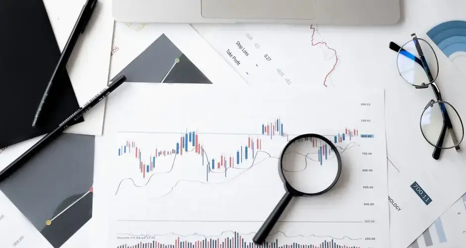 Flat lay of stock market analysis documents with magnifying glass, pens, and glasses.