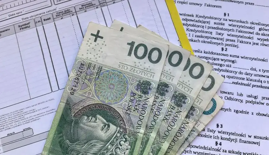 Polish 100 Zloty banknotes on VAT invoice and factoring agreement forms.