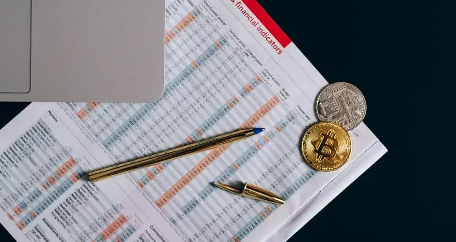 Top view of bitcoin coins on financial documents beside a laptop keyboard.