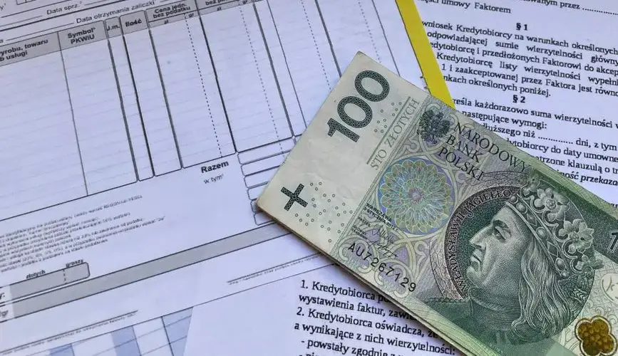 100 Polish zloty bill on top of financial documents and invoices on desk.