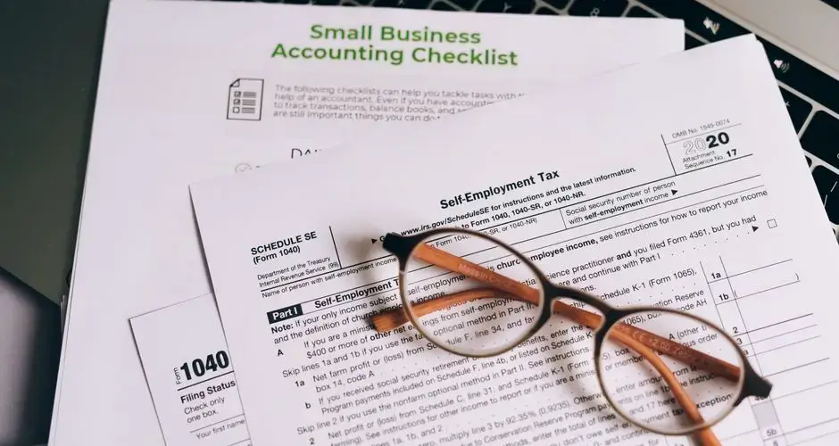 Close-up of tax forms and a small business accounting checklist on a laptop.