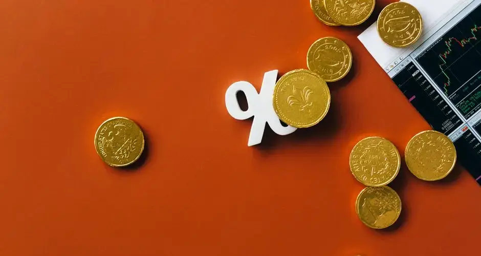 Gold coins scattered with a stock market graph and a percentage symbol on an orange background.