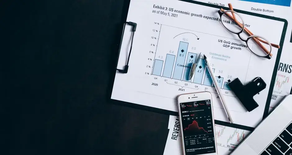 Top view of financial reports, smartphone showing stock market data, and a laptop on desk.