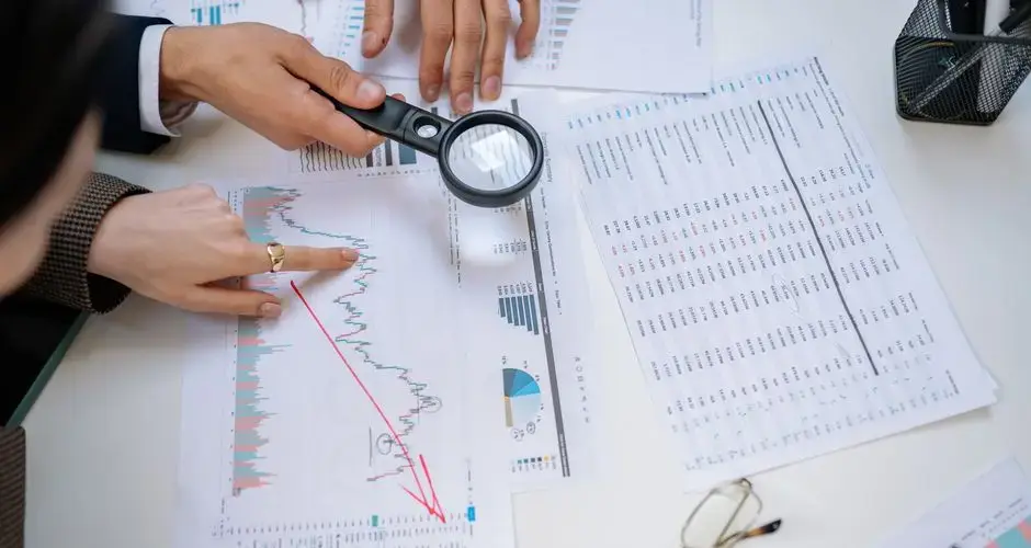 Business professionals examining financial documents with magnifying glass for detailed analysis.