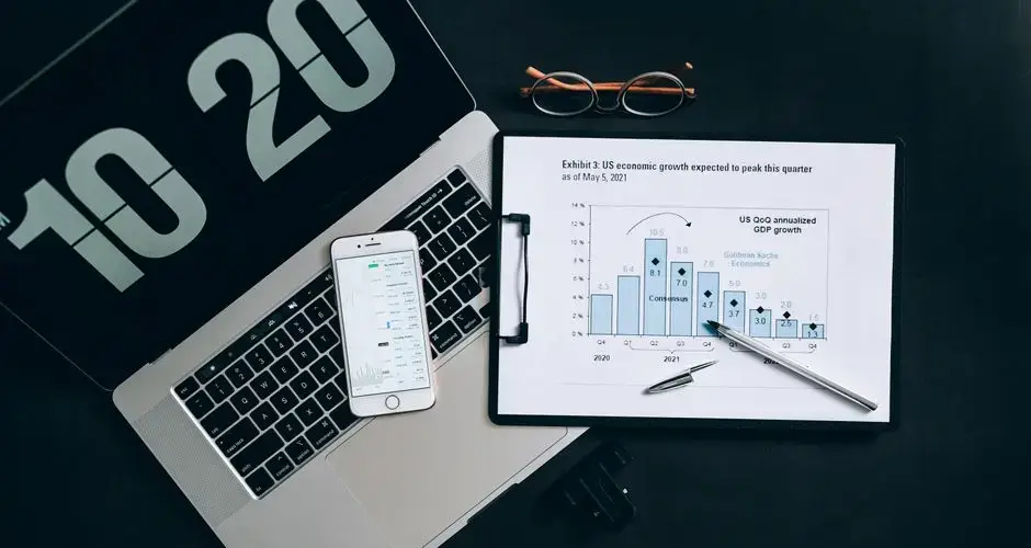 Top view of financial analysis tools on a desk including a laptop, smartphone, and graphs.