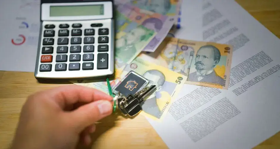 A hand holds keys next to Romanian currency, a calculator, and documents, symbolizing real estate transactions.