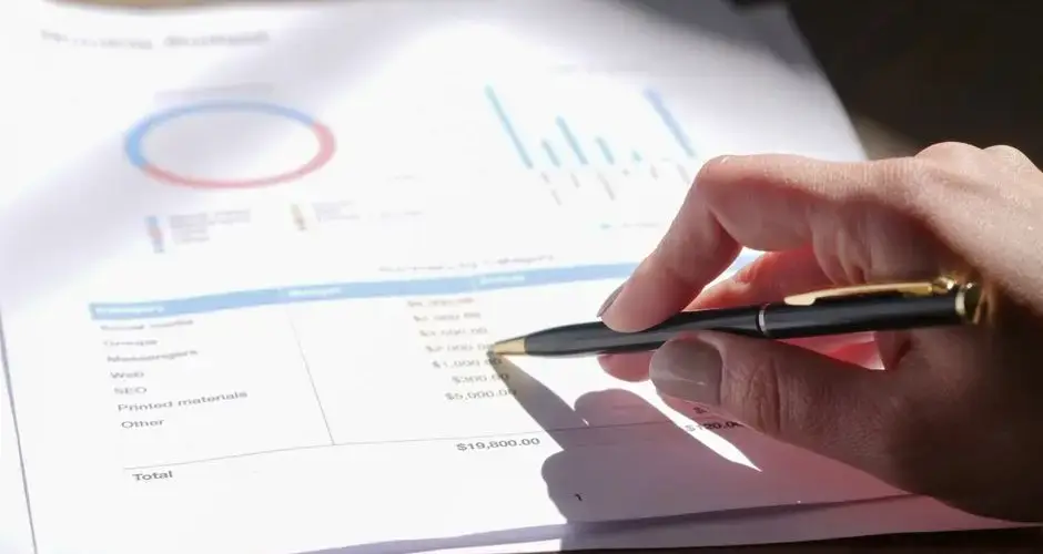 Hand holding pen, analyzing budget with charts and graph paper.
