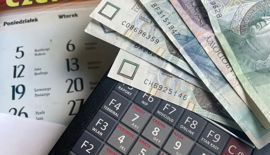 Close-up of Polish Zloty banknotes on a calculator with a calendar in the background.