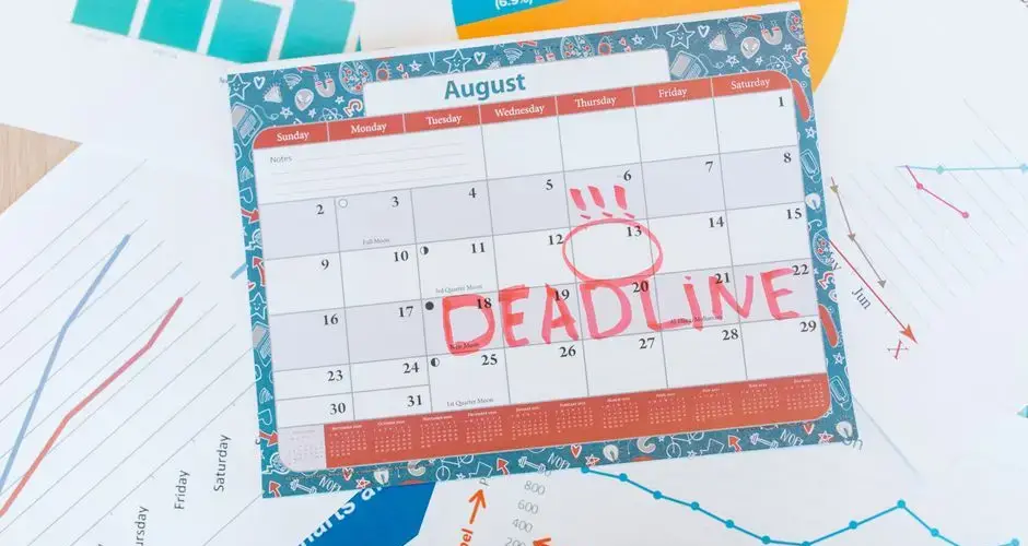 Vibrant August calendar on a desk with deadline marked in red, surrounded by graphs and charts.