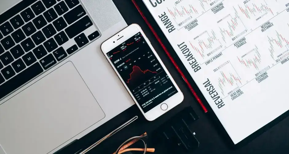 Top view of financial tools including a laptop, smartphone with stock data, and charts for market analysis.