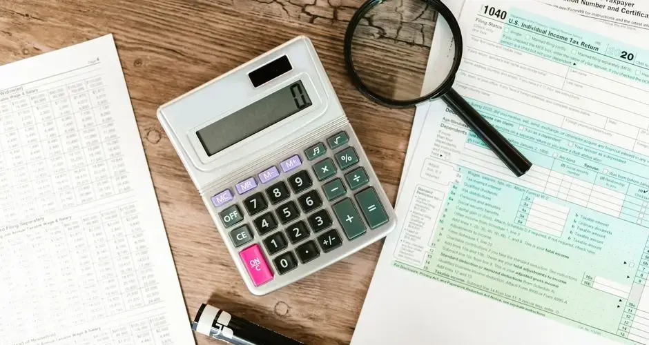 Top view of tax forms, a calculator, and a magnifying glass on a wooden surface, ideal for accounting themes.