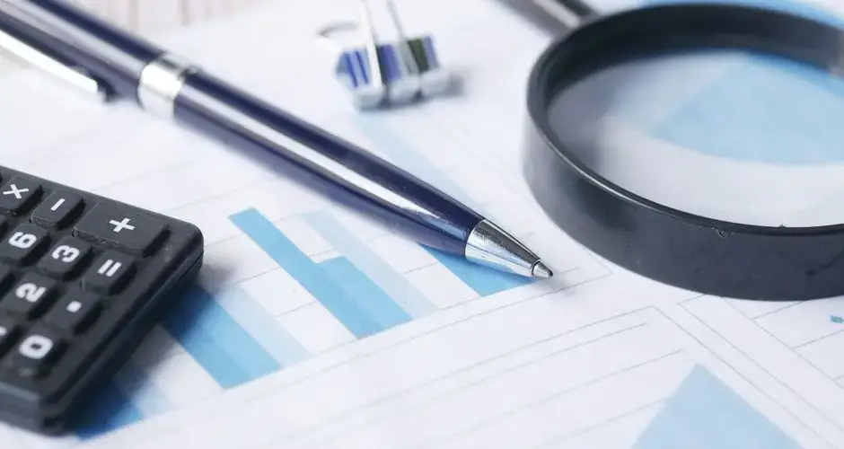 Close-up of calculator, pen, and magnifying glass on financial documents.