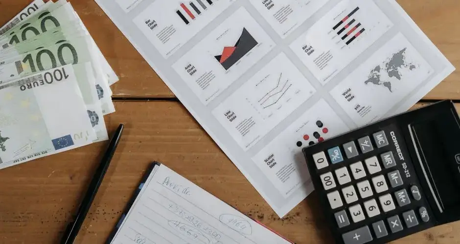 Euro banknotes, graphs, and calculator on a wooden table setup for financial analysis.