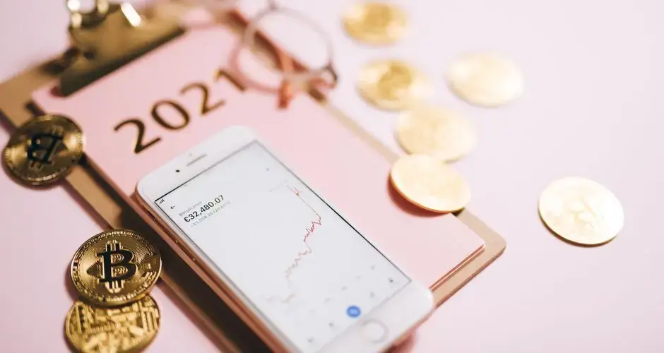 Close-up of a smartphone with crypto chart, bitcoin coins, and 2021 notepad.