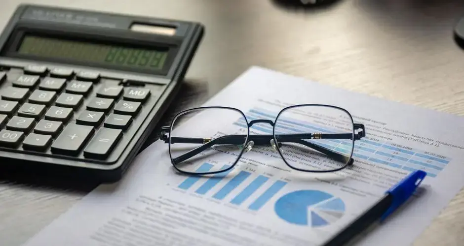 Financial document with a calculator, pen, and glasses symbolizing data analysis.