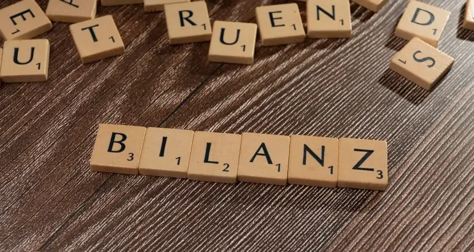 Scrabble tiles spelling 'Bilanz' on a wooden surface, symbolic of financial balance.