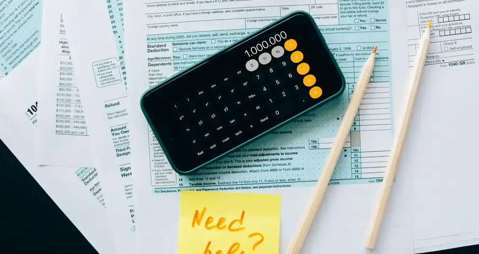 Top view of financial papers with a calculator, pencils, and a note saying 'Need help?' indicating tax or accounting assistance.