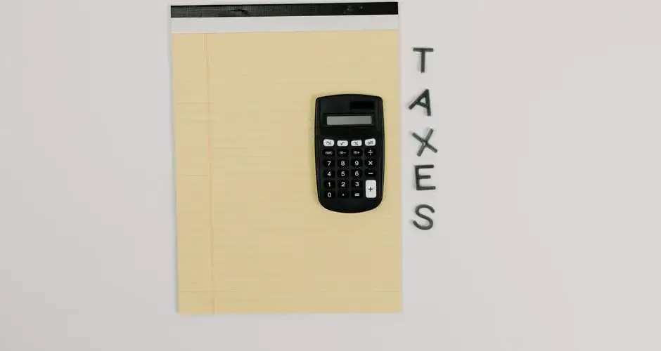 Top-down view of a calculator on a yellow notepad with 'TAXES' spelled out beside.