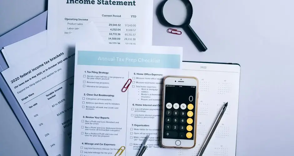 An organized desk with tax documents, checklist, and gadgets for tax preparation.