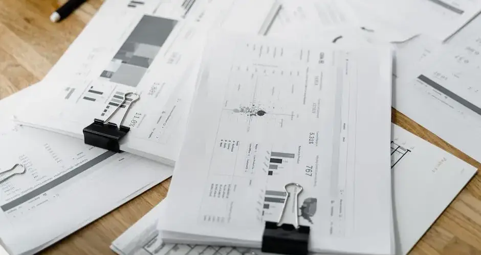 A stack of financial reports and graphs with clips on a wooden desk, highlighting business planning.