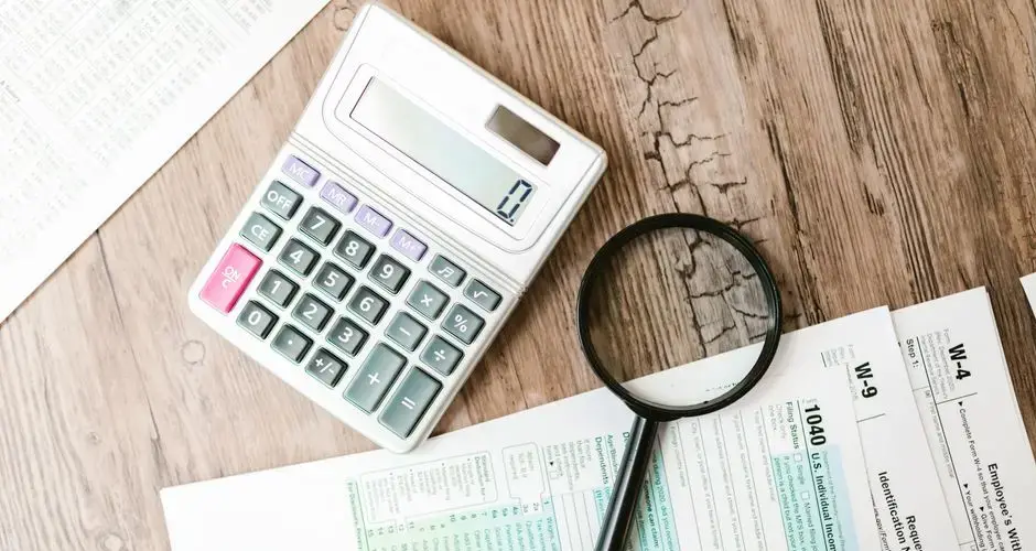 Tax forms laid out with a calculator and magnifying glass on a wooden surface, perfect for finance themes.