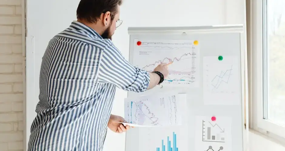 A businessman pointing at financial charts on a whiteboard, discussing stock market trends.