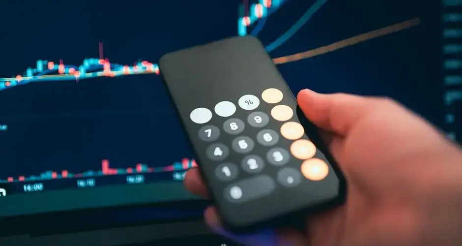 Close-up of a smartphone displaying a calculator with a financial chart in the background.