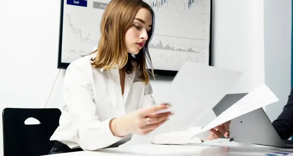 Focused woman analyzing financial reports in a modern office setting with charts and graphs.