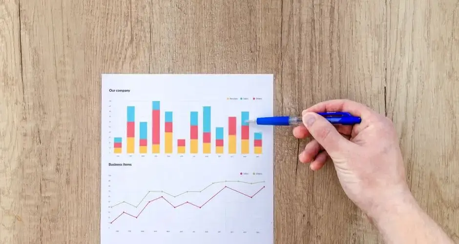 A hand points a pen at business graphs on a wooden table, highlighting data analysis.