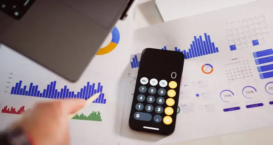 Business analytics setup with calculator, graphs, and laptop, showcasing financial insights.