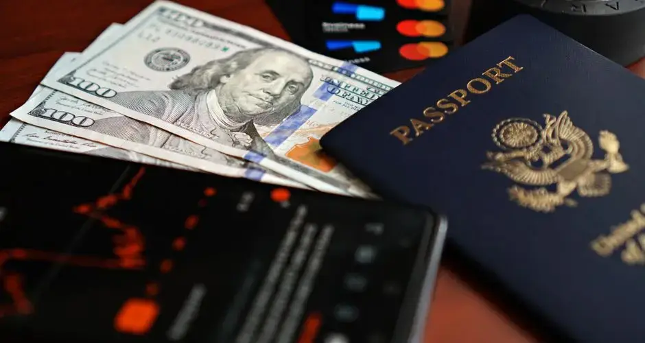 A flat lay of travel essentials including a passport, US currency, and credit cards on a table.