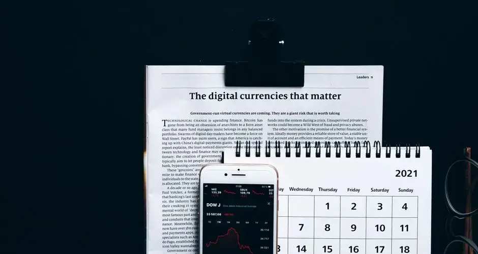 Digital currencies article with smartphone stock market app and calendar on black surface.