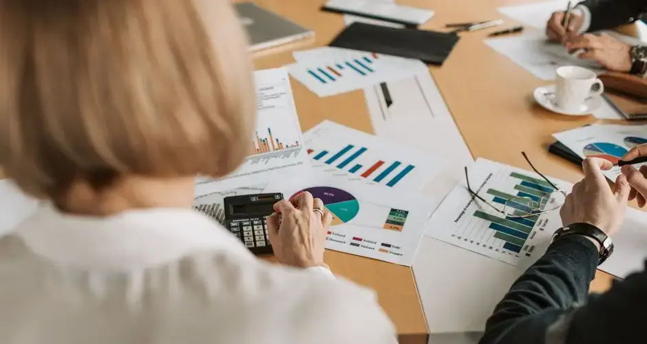 Overhead view of professionals discussing financial graphs and using calculators in an office setting.
