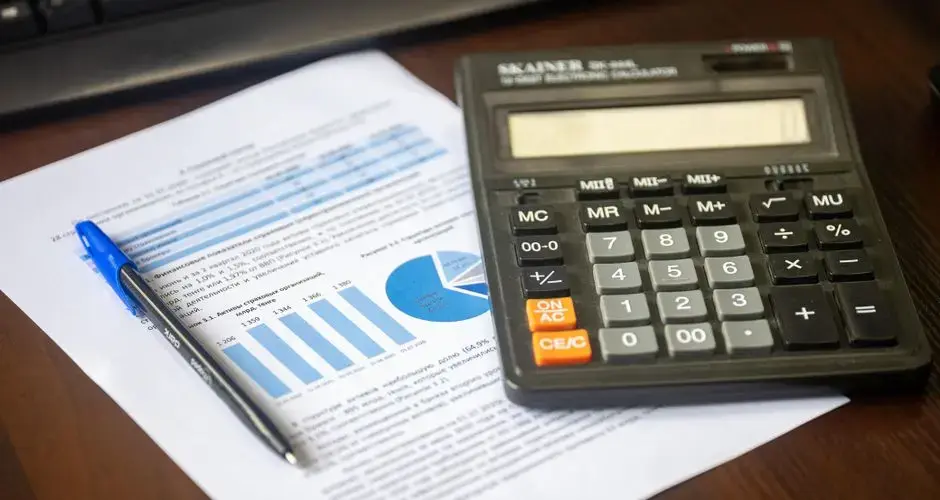 Close-up of a calculator, pen, and financial report on a wooden desk.