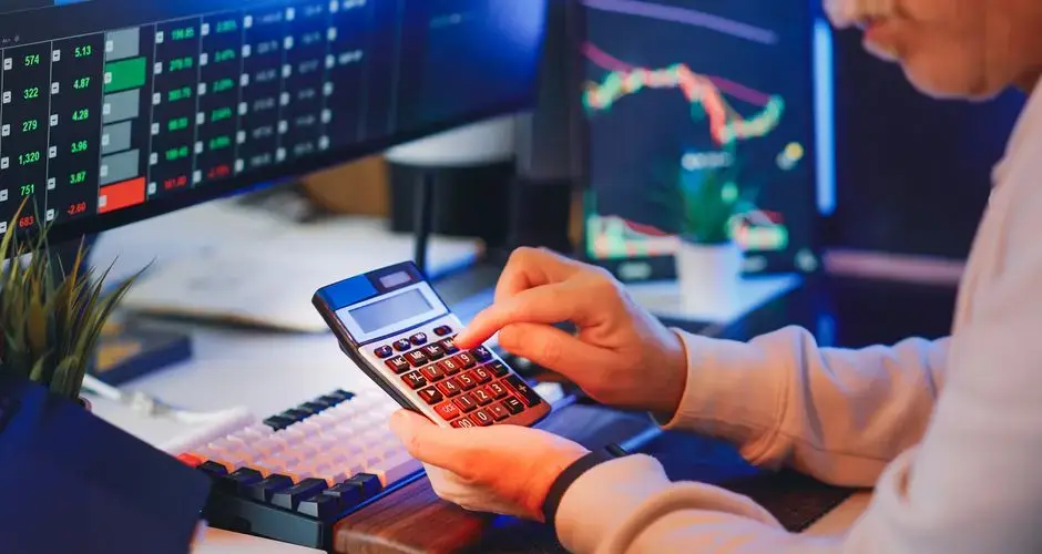 Person using a calculator in a digital office for stock market analysis.