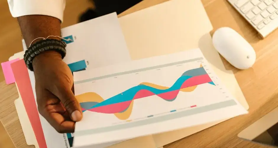 A person's hand holds a printed business graph paper on a desk with office supplies.