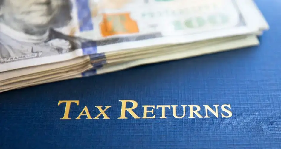 Close-up of tax returns folder beside a stack of American dollars, representing finance and accounting.