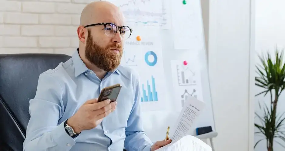 Bald man with eyeglasses reviews financial data in office with diagrams.