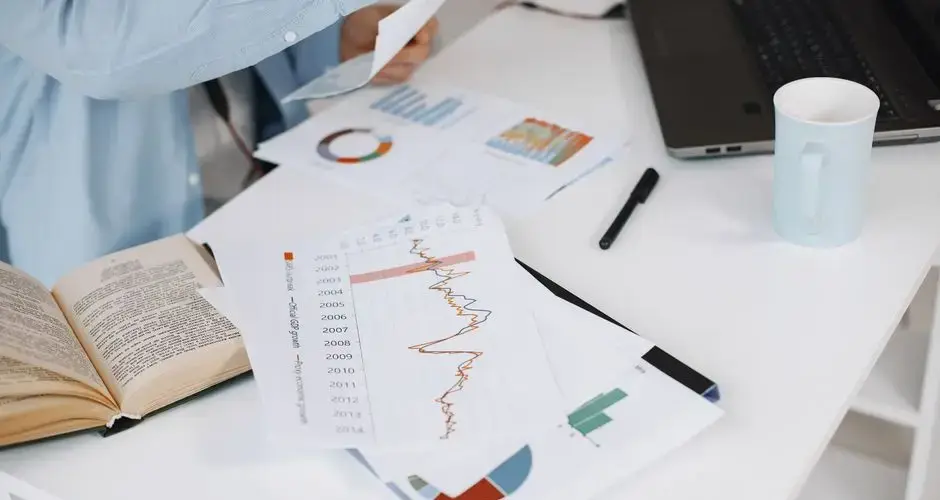 Office workspace with data charts, book, and laptop on a white desk.