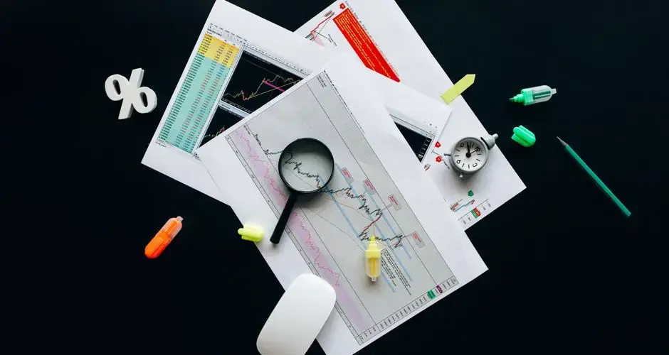 Overhead view of an office desk with financial documents, a magnifying glass, and stationery items, suggesting business analysis.