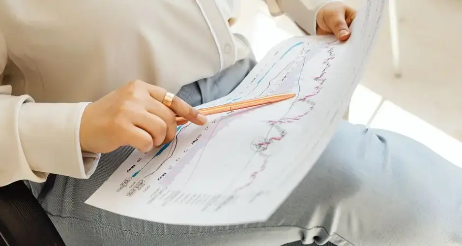 Close-up of hands holding and analyzing finance charts with pen.