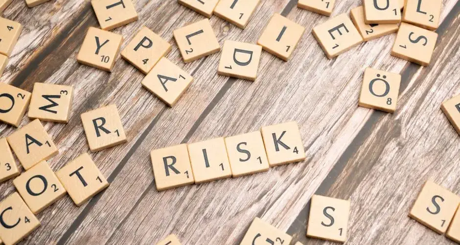 Scrabble tiles spelling out 'risk' scattered on a rustic wooden background, symbolizing uncertainty.